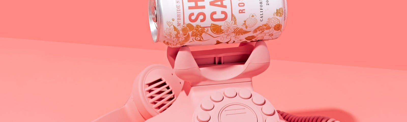 pink old telephone with a soda can that says ‘she can’ against a pink background