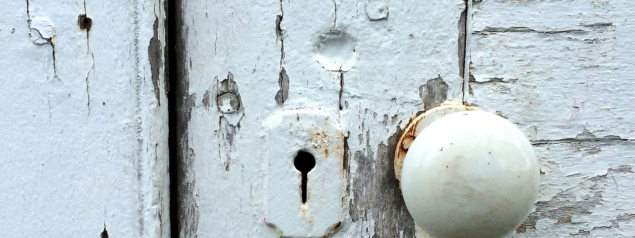 Close up image of old paint encrusted door’s keyhole next to a doorknob.