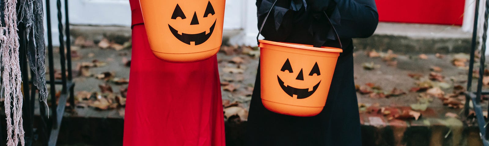 Two kids in Halloween costumes holding pumpkin buckets