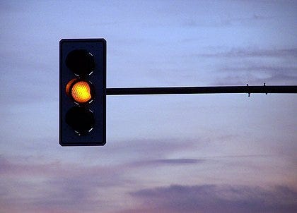 Imagem de um semáforo em luz amarela, contra um fundo de céu azul cinzento