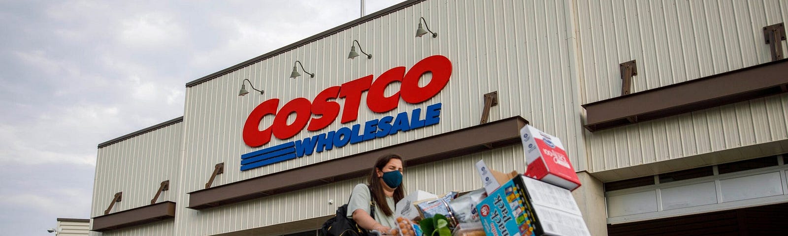 A masked customer pushing a shopping cart in front of a Costco.