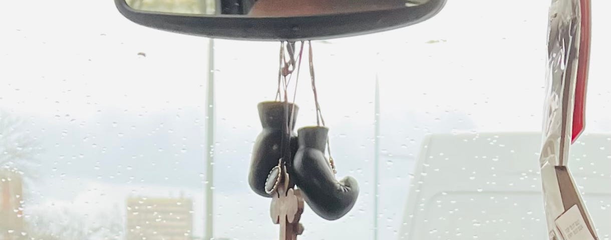 A big wooden cross and a pair of mini boxing gloves hanging from a rearview mirror