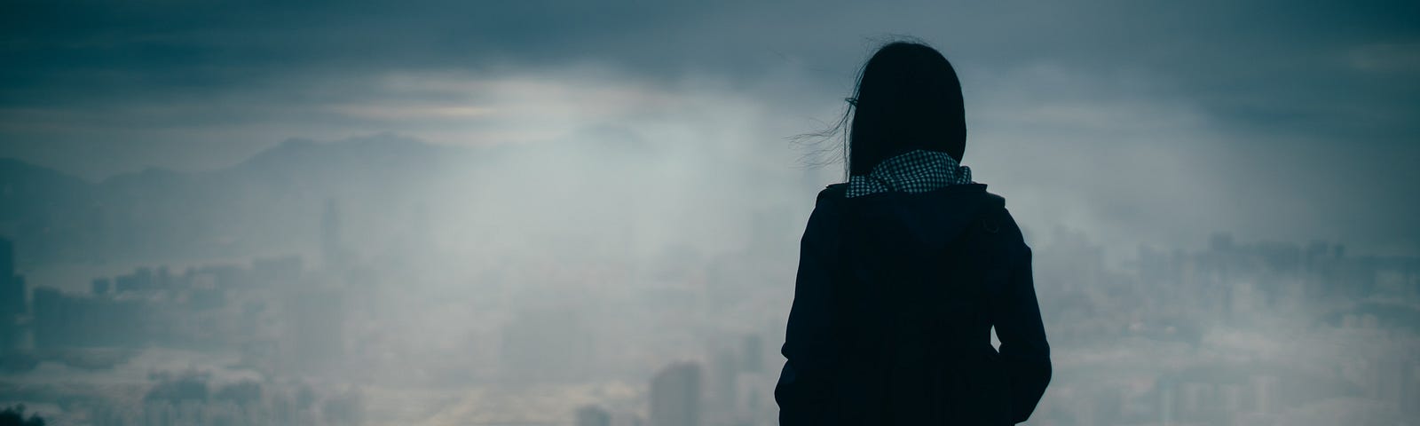 Silouette of woman standing on a hill looking at bleak landscape.