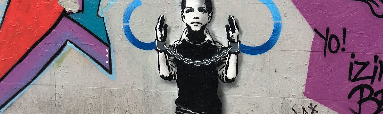Graffiti of a boy with his hands raised in handcuffs and a cloud outline encircling his head representing ideas.