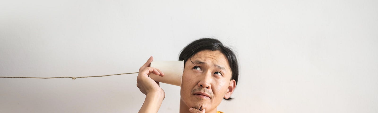 Pensive ethnic man listening to answer in paper cup phone