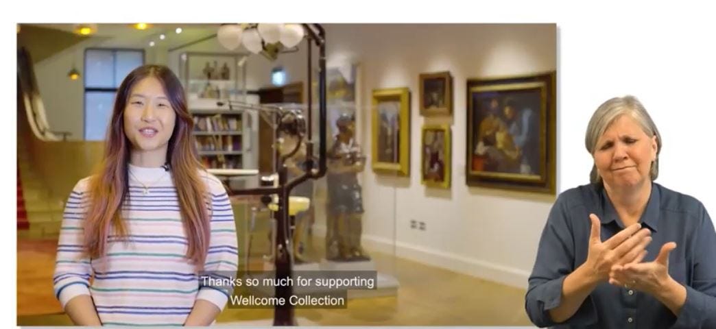A video screenshot. A smaller square shows a woman of South East Asian heritage with long dark hair, wearing a light stripey jumper, standing in the Reading Room at Wellcome Collection, in the middle of speaking. Some captions show she is saying “Thanks so much for supporting Wellcome Collection”. This square is set on a white background, next to this is a white woman with grey hair, wearing a dark shirt, in the middle of interpreting in British Sign Language.