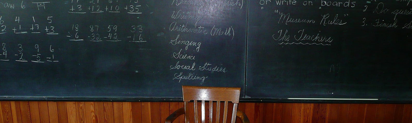 Image of books spread across a teacher’s desk in front of a classroom chalkboard.