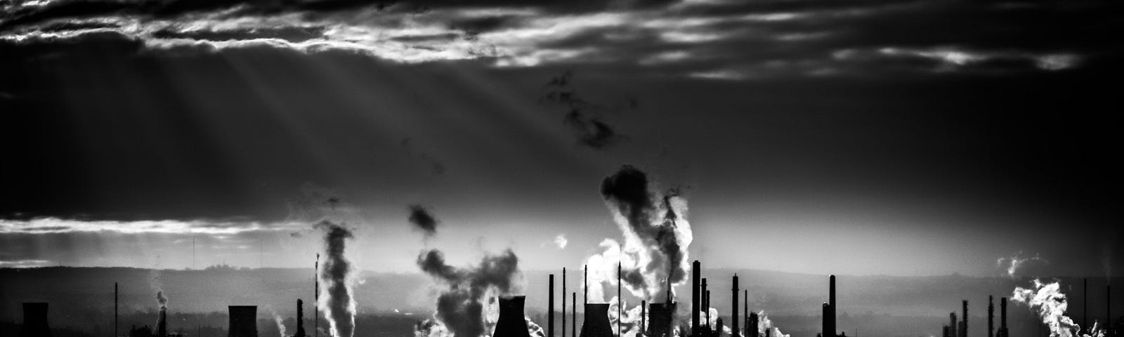 Silhouette of a power plant with cooling towers and trails of clouds.