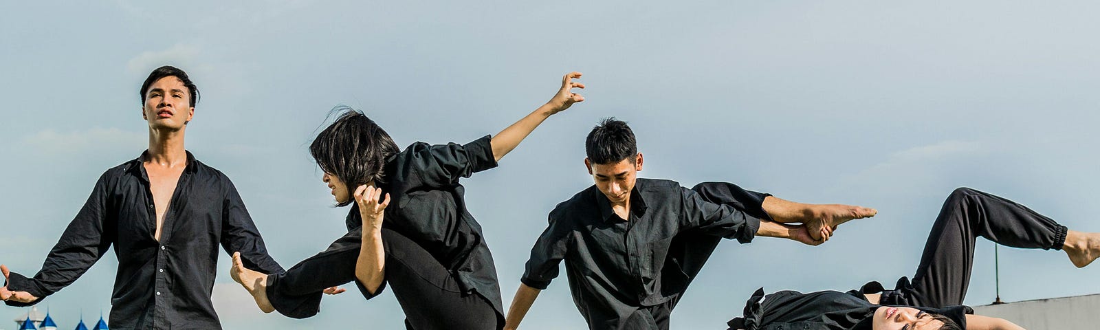 6 dancers dressed in black posing in stances with their legs lifted and arms bent