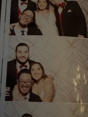 Wedding photo booth. Jonathan is seated in his wheelchair, wearing a tuxedo. His nephew stands behind him in a tuxedo, and Jessica, the bride stands beside Jonathan.
