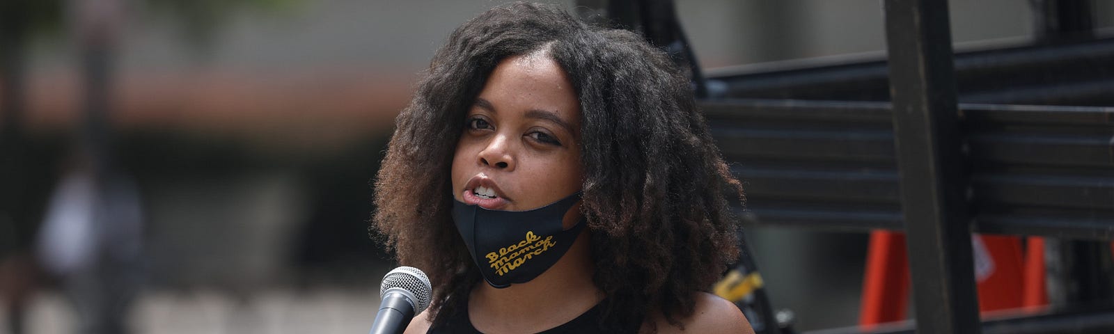 Woman speaks at microphone during a protest. Photo by Kevin Banette.