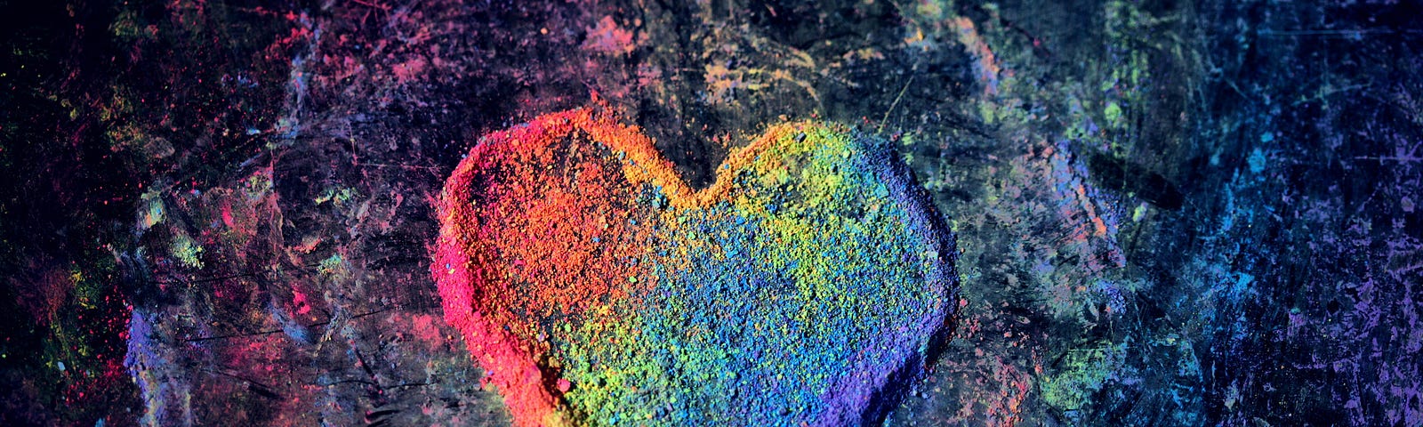 Image of a rainbow-colored heart drawn in chalk powder on a chalk- and paint-splashed surface.