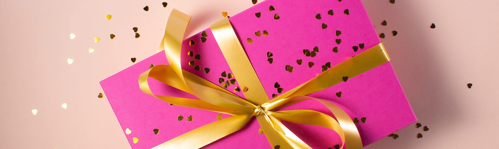 Pink wrapped gift with a gold bow and confetti