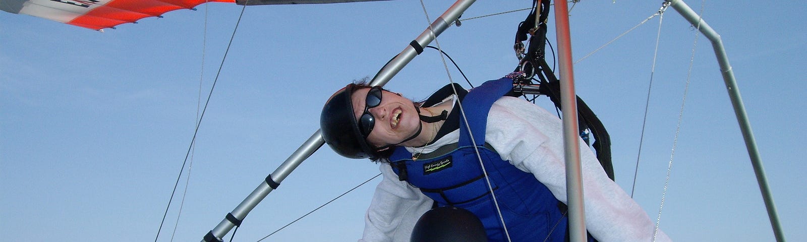 I dressed in a blue vest, and black goggles, suspended from a hang glider and above the instructor in midair.