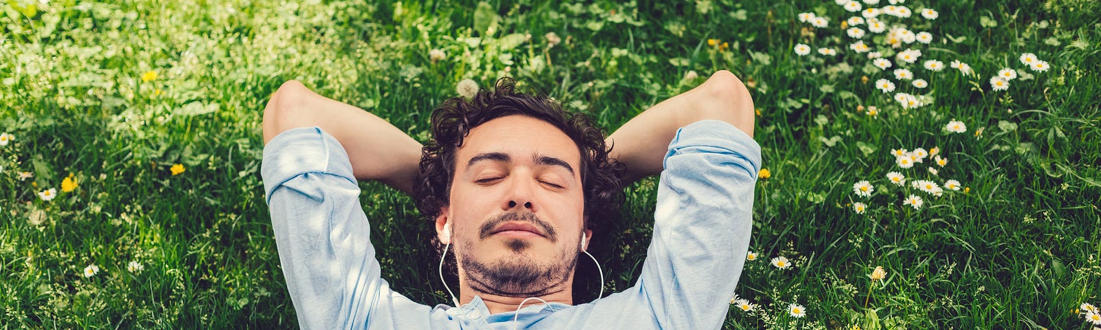 Relaxed man lying down at the meadow and listening to music
