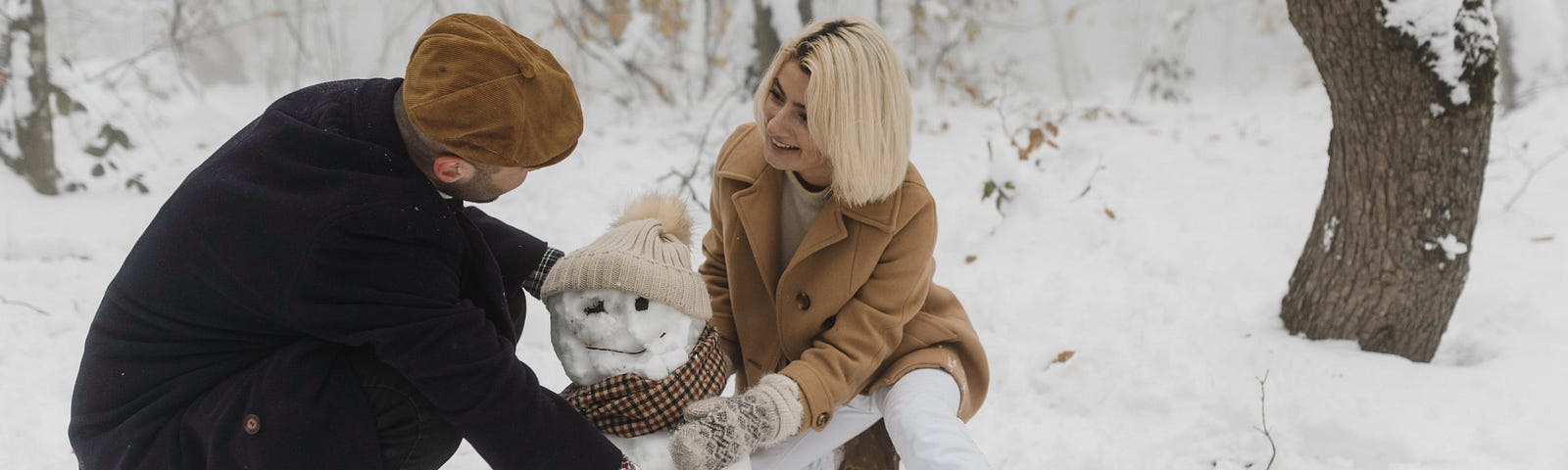 A couple builds a snowman in the cold