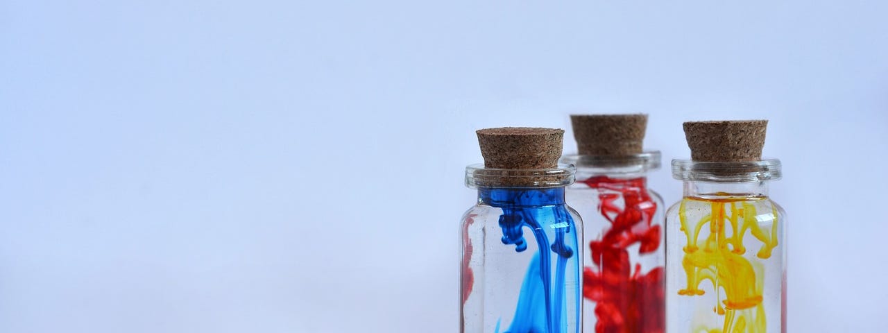 Three small flasks sealed with corks. From left to right: blue, red and yellow dye are being slowly mixed in each one.