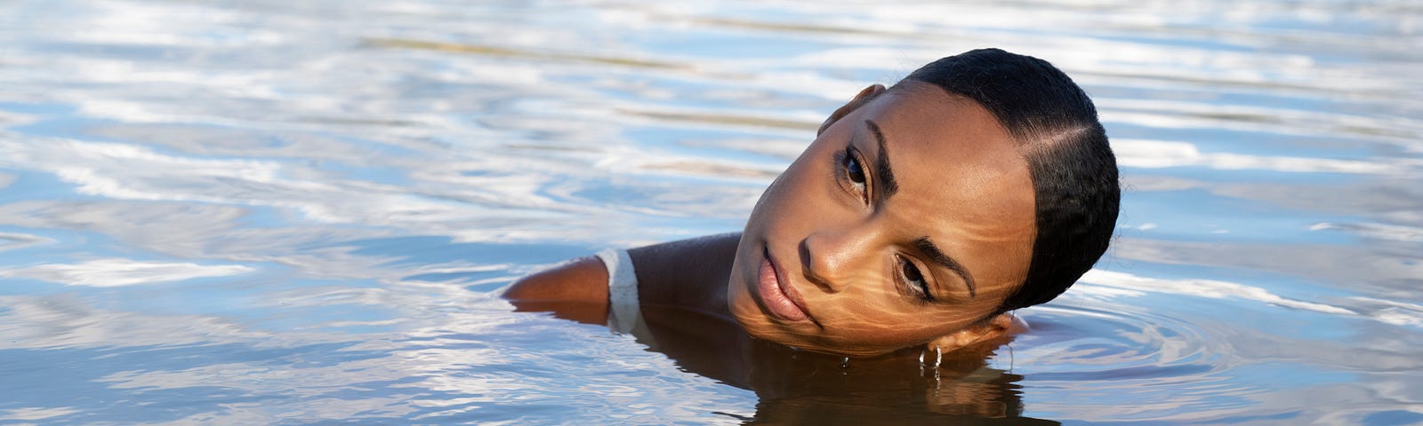 Black girl in the ocean holding her face above water.