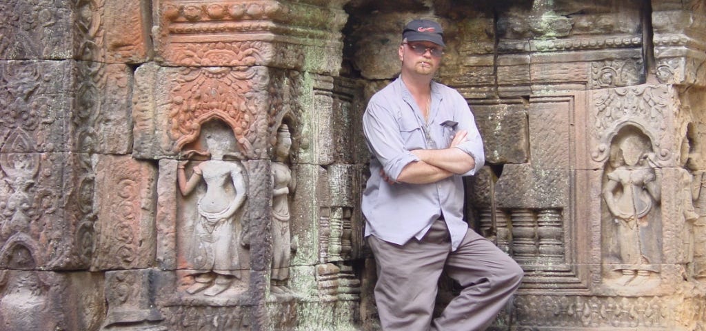 man standing in front of bas relief carvings on wall of Angkor Wat complex in Cambodia.
