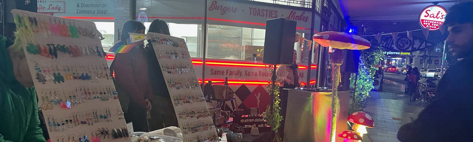 Market stall selling jewelry next to a DJ with prop mushrooms.