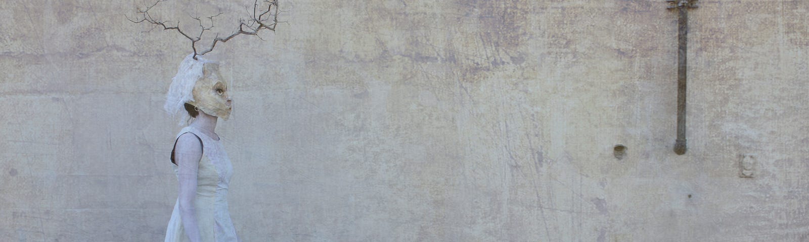 A masked figure in white walk along an old, wall, textured in shades of off-white and beige.