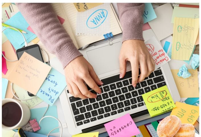 A person typing on a keyboard atop a cluttered desk.