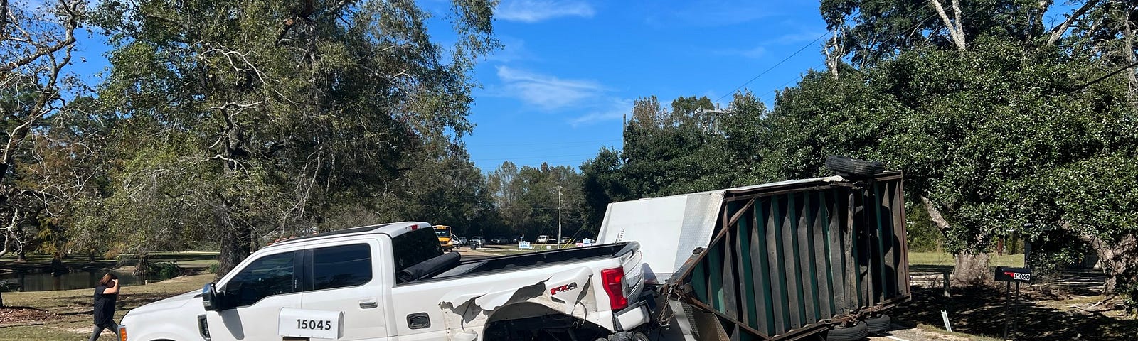 One-ton dually pickup truck after the wreck with the driver side rear wheels rolled under the truck and a 7x16 foot box trailer laying on it’s side blocking the road.