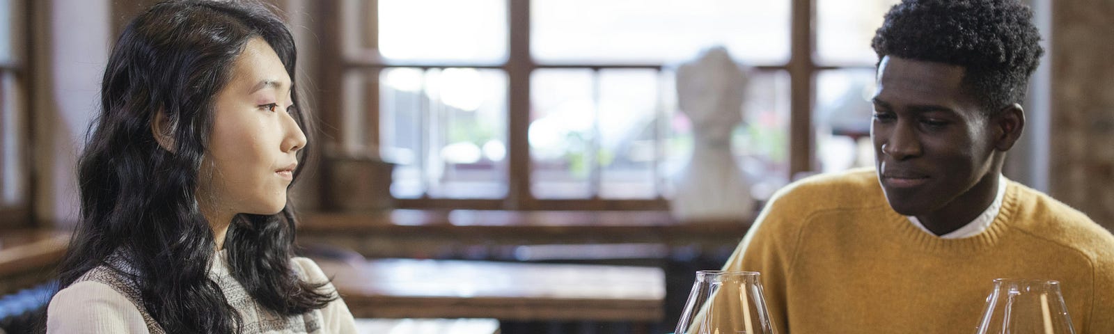 Asian woman and black man sitting at a table and each drinking a cup of wine