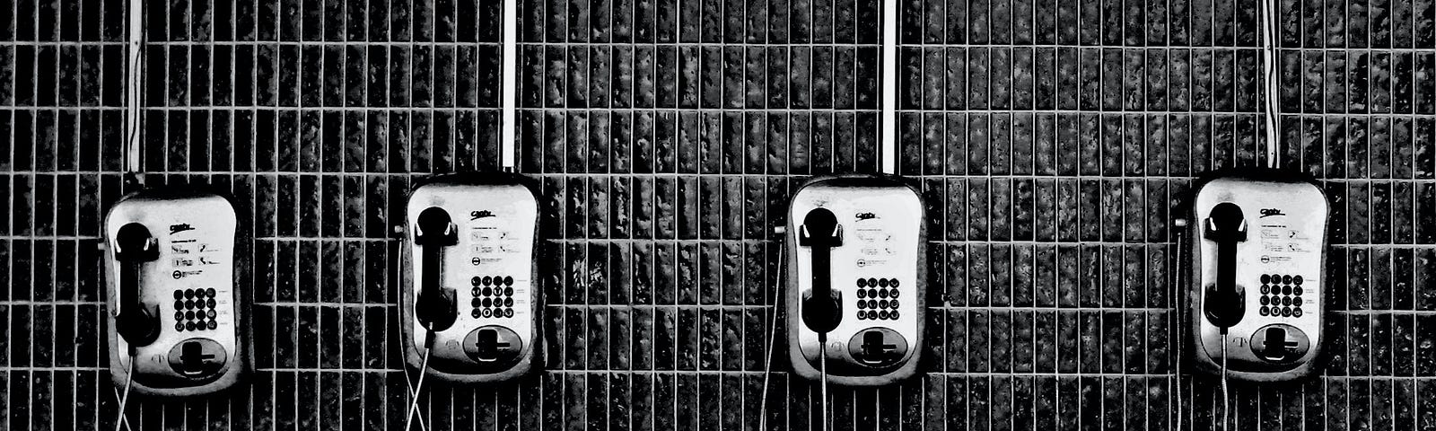 Four public telephones on a tiled subway wall.