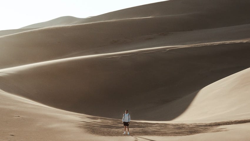 Picture of a man alone in a dessert with traces of footsteps
