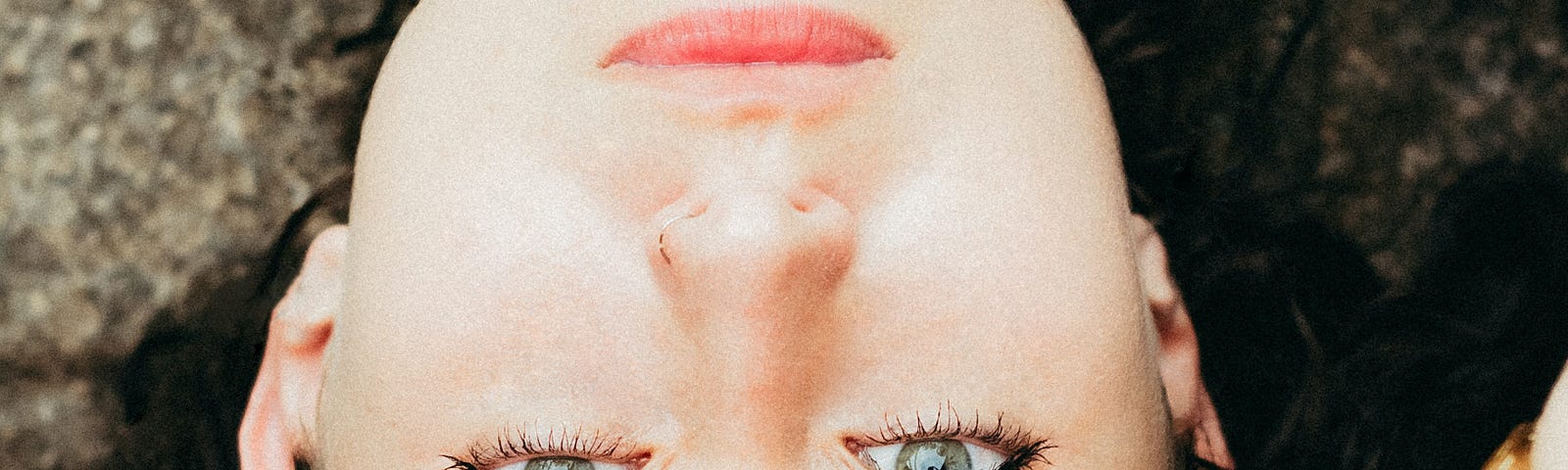 Close up of woman’s face. Picture is upside down. Her hand is on her forehead. She wears a white dress with red flowers.