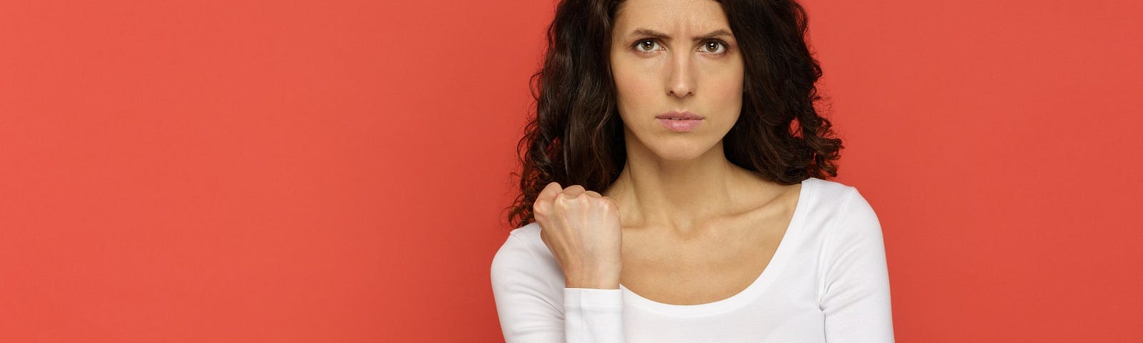 A woman with an angry face holds up a balled fist against a red background.