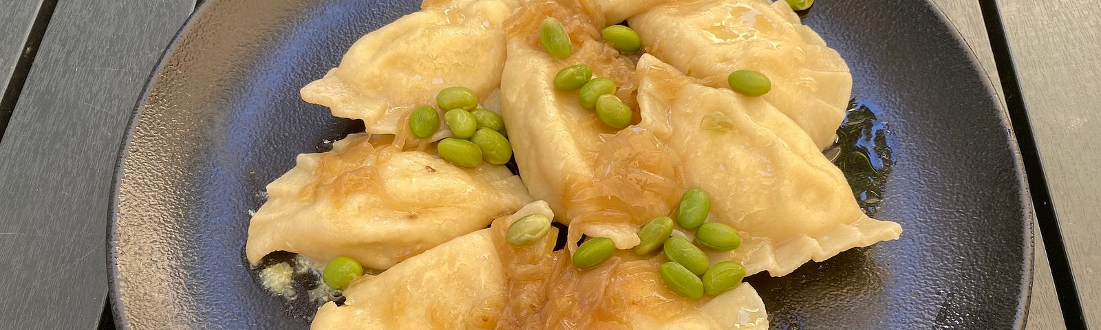 A plate of delicious pierogie ruskie, topped with fried onion and edamame beans