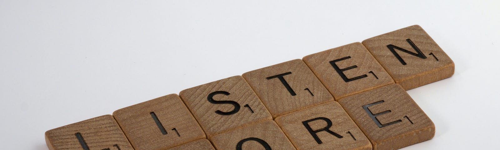 Wooden Scrabble tiles spelling out “Listen more.”