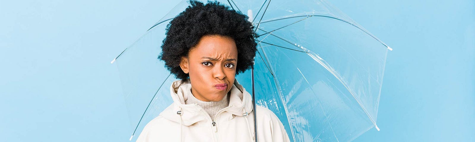 Young black woman with short hair holds an umbrella. She has an angry, yet pensive look on her face.