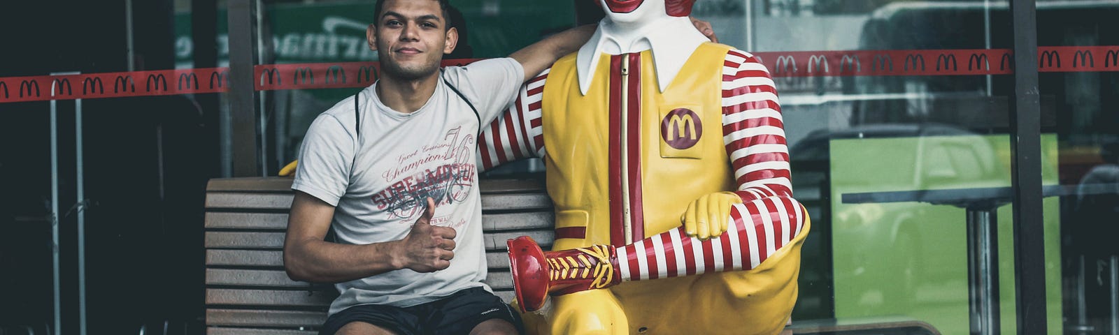 A guy seat with Ronald McDonald on a bench