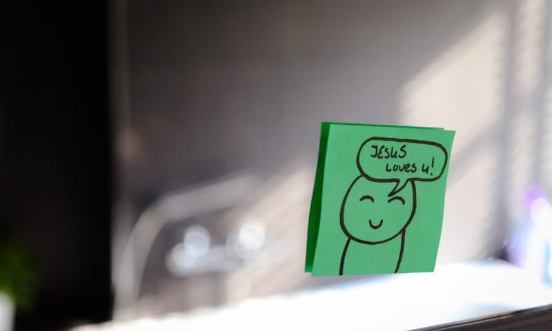 Image of a green post-it note stuck on a window with the message” Jesus Loves U (Jesus Loves You).