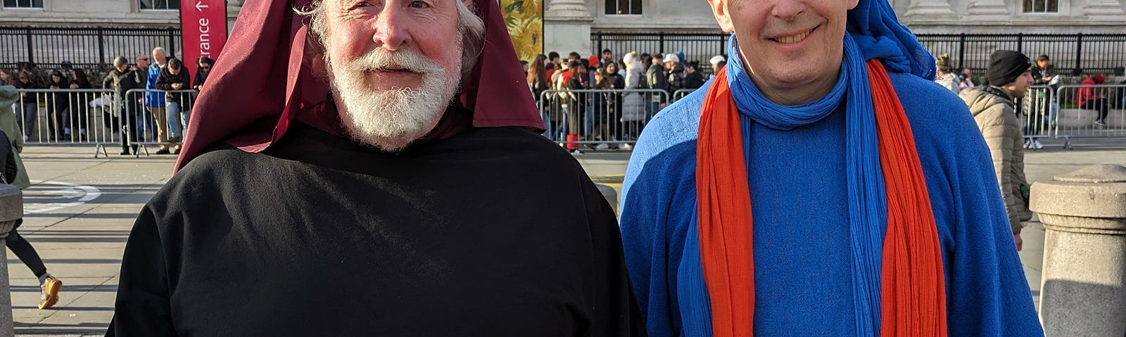 Two men, one dressed in black with burgundy headdress the other in blue and red.