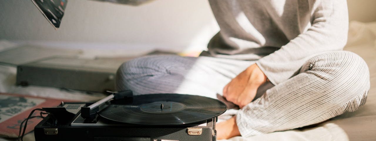 Photo of a woman sitting on a bed with a record player and albums.