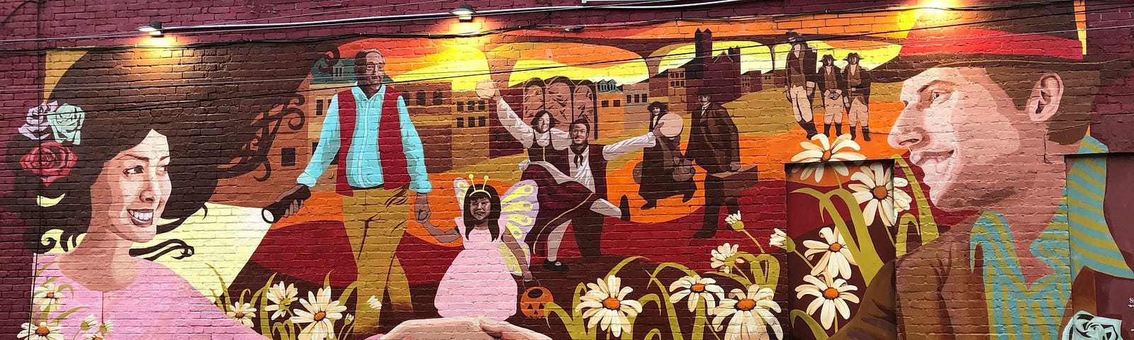 Mural on a brick wall showing a couple holding hands, daisies, and a line of people depicting various time periods, from the 1770s to the present