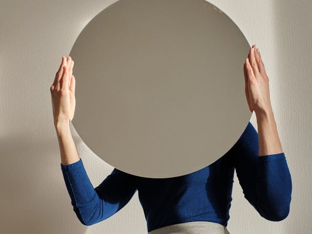 Woman in blue shirt, face blocked because of large circular mirror she is looking at