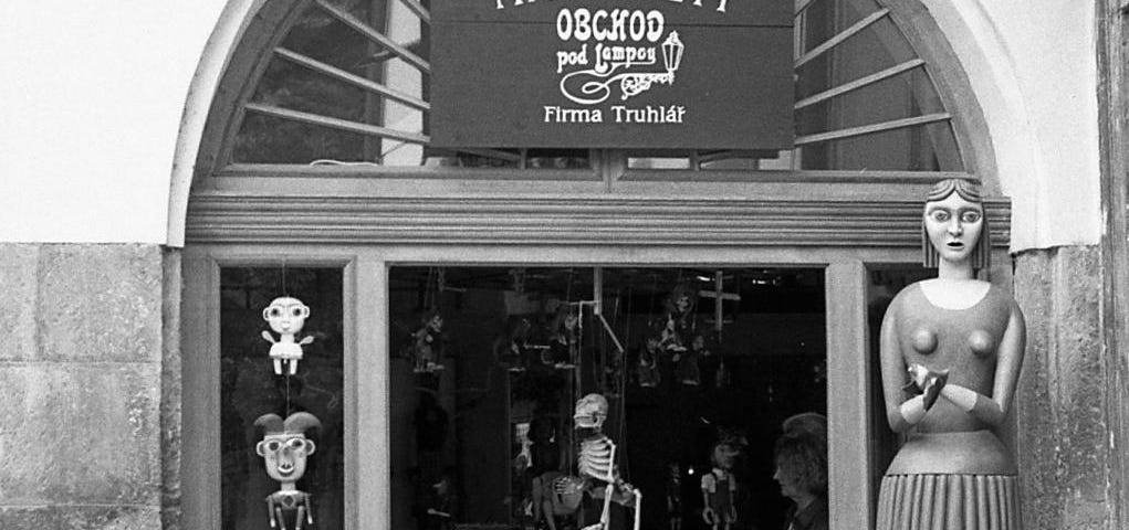 Black and white photo of lovers outside a marionette shop, a skeleton marionette shows hanging in the background