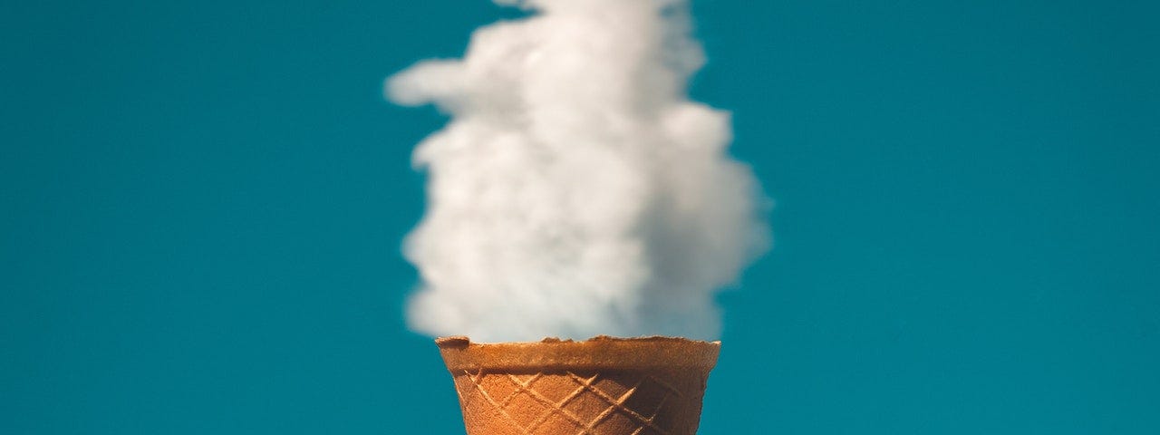 Man holding an ice cream cone under a cloud. The back ground is blue.