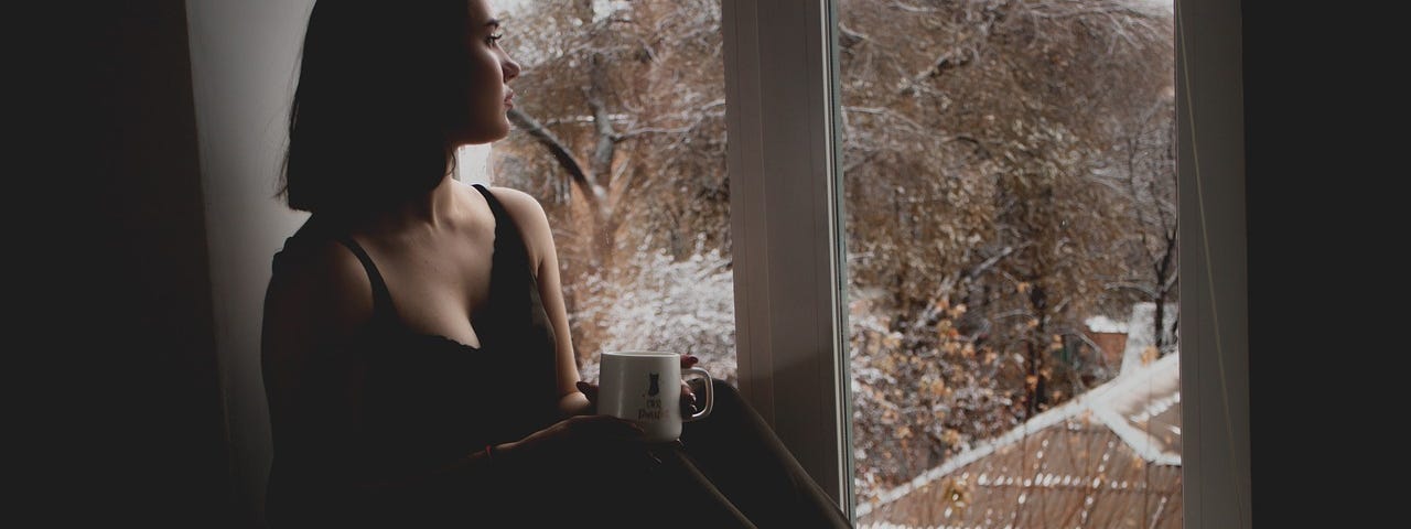 Young woman sits on first or second floor windowsill looking outside