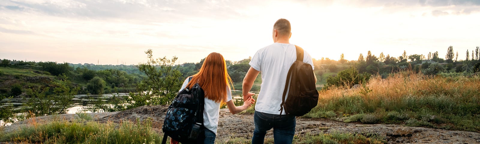 A couple walk hand-in-hand through a green landscape, beneath a blue sky.