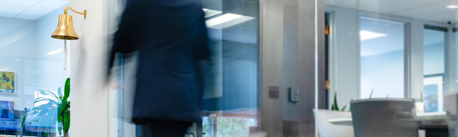 A blurry image of a man walking very quickly through an office.