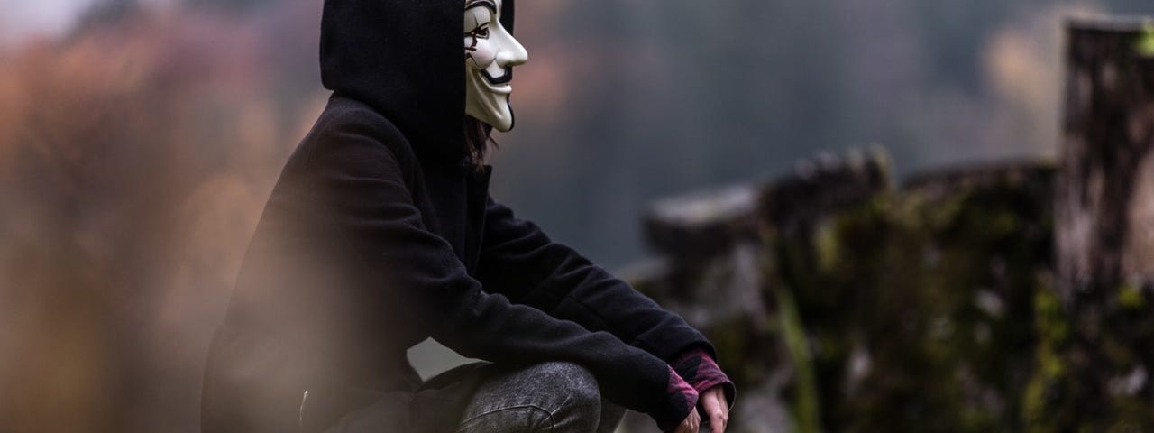 Boy with Guy Fawkes mask sitting down, looking to the distance
