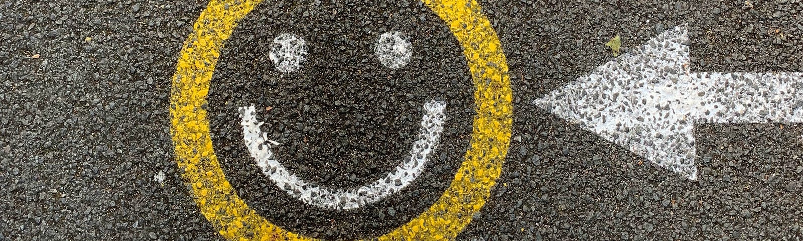 Person standing on a street with an arrow pointed to a painted yellow and white smiley face.