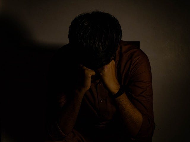 a person crying into their hands in a dark room.