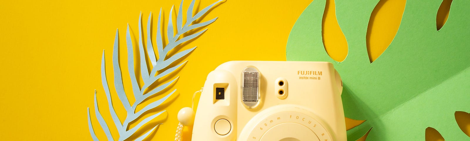 a fuji camera beside two green paper cutouts of leaves, on a yellow background